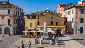 A plaza with a statue, outdoor seating, and buildings with balconies. - La Casina Del Pescatore On the Beach (Pietrasanta)