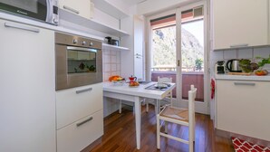 Une cuisine compacte avec des meubles blancs, un four encastré et un four à micro-ondes. Une table à manger avec des chaises est placée près d’une fenêtre donnant sur un paysage montagneux.
