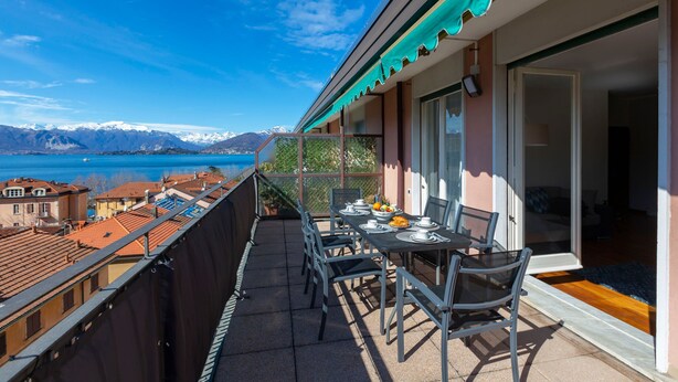 Un balcon avec une table dressée pour deux personnes, offrant une vue sur un lac et des montagnes.