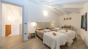A bedroom with two beds, a bedside table, a nightstand, and a small desk with a chair. There is a window with curtains, a wall-mounted TV, and a ceiling with exposed beams. - Arco Rocks 3 in Arco (Arco)