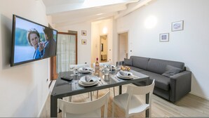A modern dining area with a glass table, white chairs, and a grey sofa. A flat-screen TV is mounted on the wall. - Arco Rocks 3 in Arco (Arco)