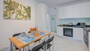 A modern kitchen with white cabinets, a dining table set with plates, glasses, and a bottle, and a large painting on the wall. - Casa dei Nonni in Arco (Arco)