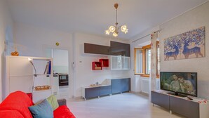 A modern living room with a red sofa, a TV on a white stand, and a kitchen in the background. - Casa dei Nonni in Arco (Arco)