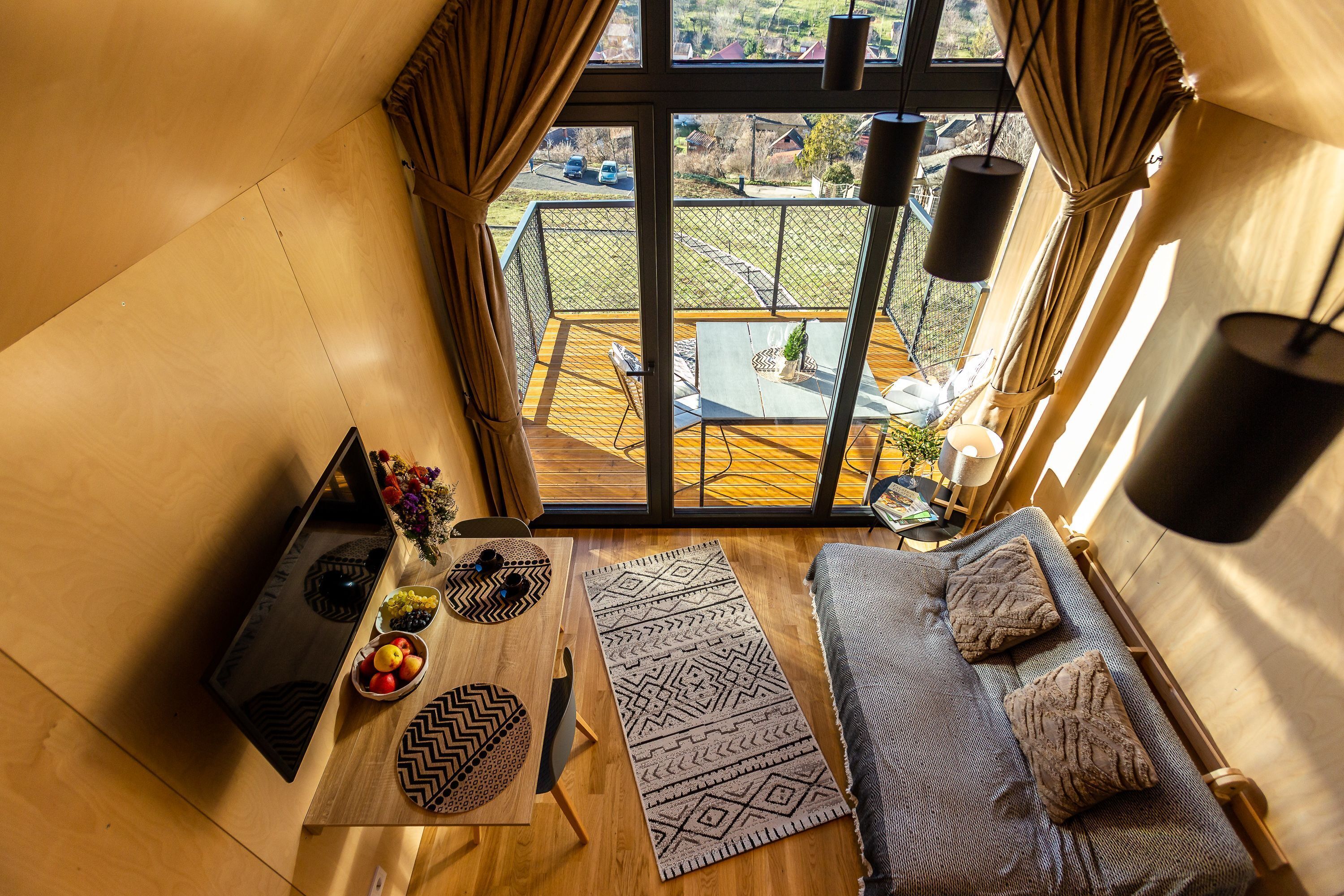 A compact living space with a balcony, a dining table with a vase of flowers, and a sofa with cushions.