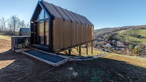 Une cabane moderne en bois, dotée d’un toit à pente, de grandes fenêtres et d’une petite terrasse.