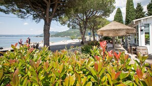 A coastal area with a beach, trees, and outdoor seating. - Margherita Near Lake-child Friendly (Toscolano Maderno)