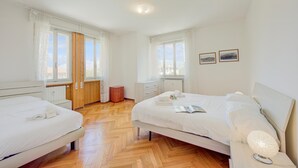 A hotel room with two beds, wooden flooring, white walls, and large windows. - Margherita Near Lake-child Friendly (Toscolano Maderno)