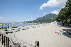 A beach with rows of sun loungers and umbrellas, a wooden pier, and a mountainous backdrop. - Margherita Near Lake-child Friendly (Toscolano Maderno)
