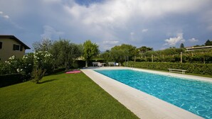 Una piscina rectangular con superficie de agua azul cristalina, rodeada por un césped cuidado y una variedad de árboles y arbustos.