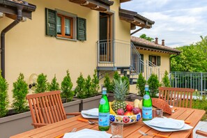 A wooden table set outdoors with a bottle of Pellegrino water, a bowl of fruit, and a pineapple. - Il Lago Blu Loft With Pool (Castelveccana)