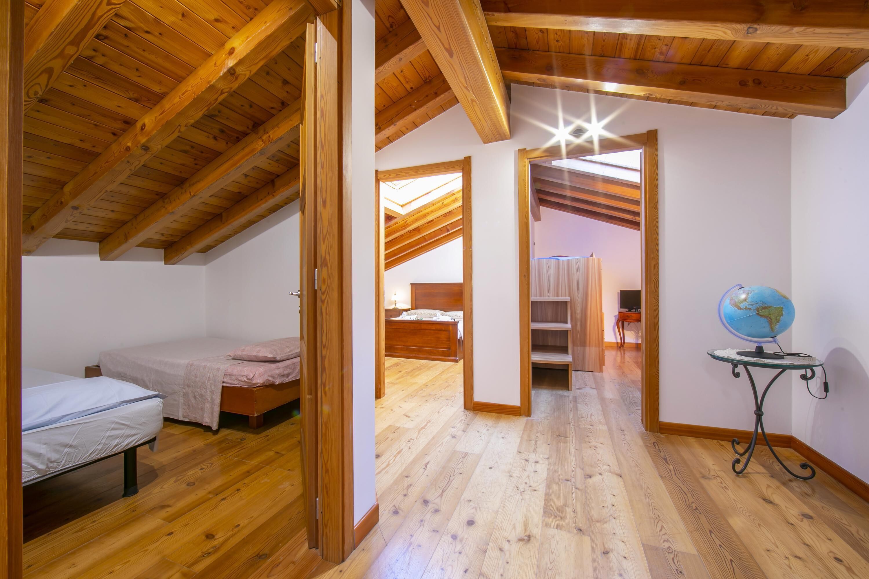 A room with wooden beams, a bed, a desk with a globe, and a skylight.