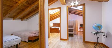 A room with wooden beams, a bed, a desk with a globe, and a skylight.