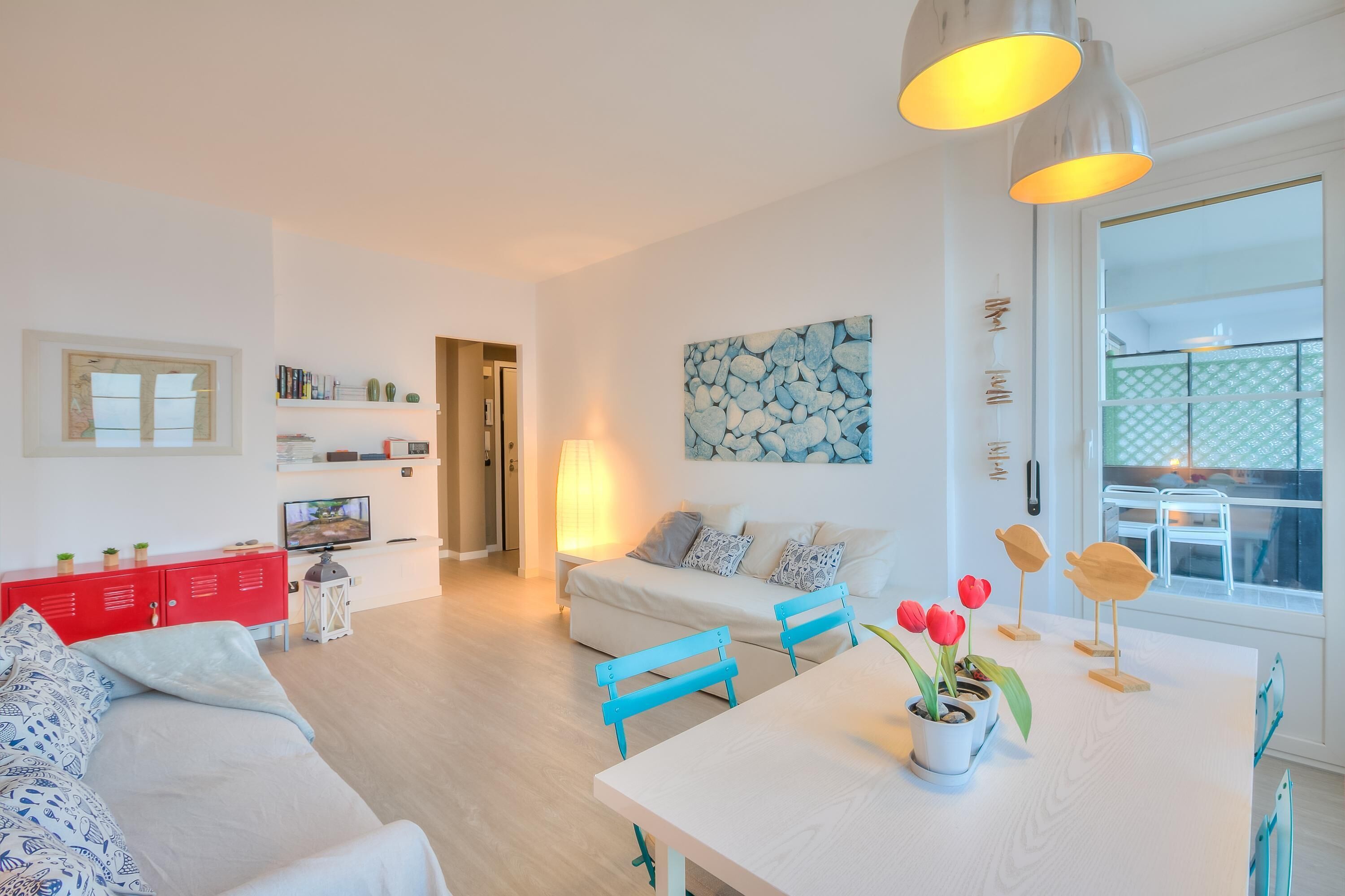 A modern living room with a sofa, a dining table with chairs, a TV, and a kitchen area in the background.