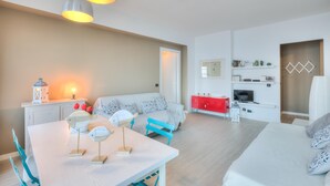 Un salon moderne et bien éclairé, comprenant un coin repas, un ensemble de canapés et un meuble rouge abritant un téléviseur.