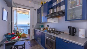 Une cuisine moderne avec des meubles bleus, une cuisinière à gaz et une vue sur la mer par une grande fenêtre.
