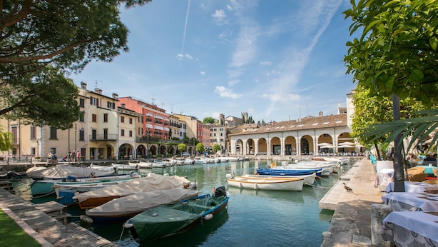 A marina with boats docked, a stone wall, and buildings with arches in the background. - Appartamento di Tommaso (Desenzano del Garda)