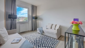 A modern living room with a sofa, a coffee table with a vase of flowers, a black and white patterned rug, and a view of buildings through a window. - Appartamento di Tommaso (Desenzano del Garda)