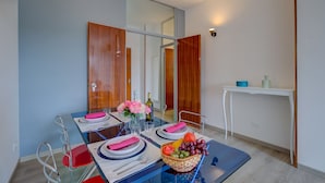 A dining area with a glass table, red and silver chairs, a white console table with a blue bowl and a bottle, and a mirror reflecting the room. - Appartamento di Tommaso (Desenzano del Garda)