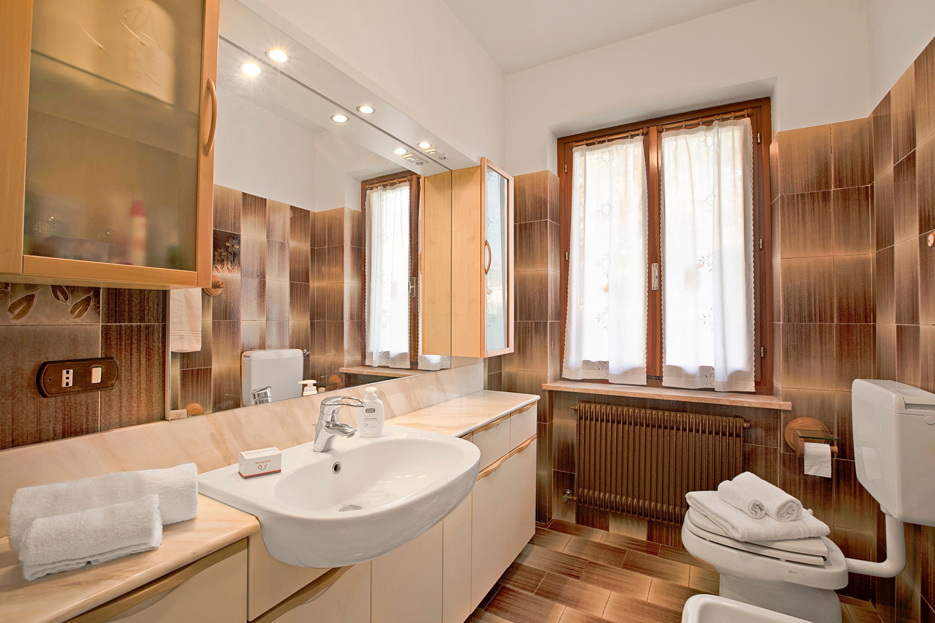 A modern bathroom with a large sink, mirror, and wooden cabinets.