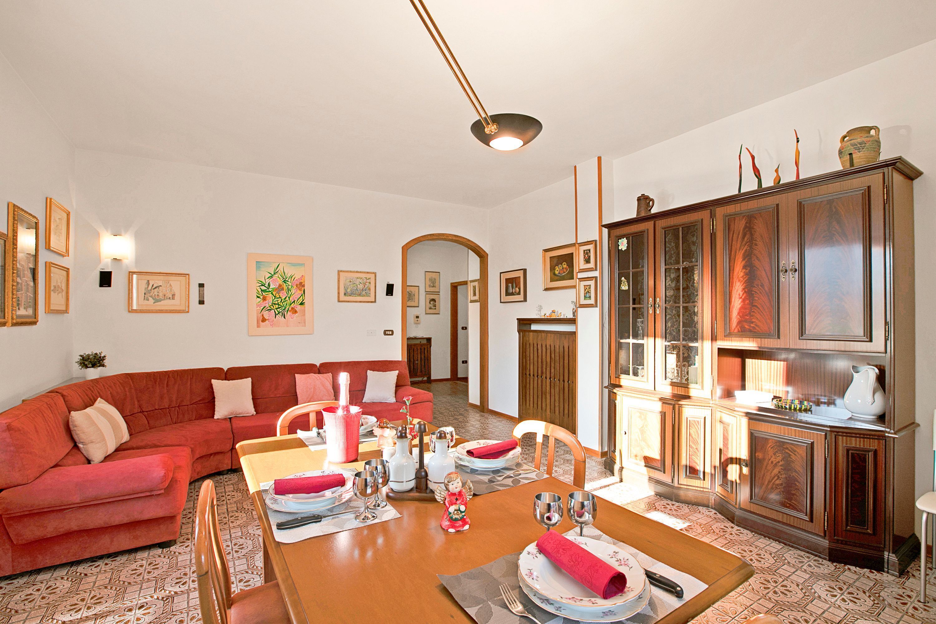 A living room with a red sofa, a dining table set for four, and a kitchen area with wooden cabinets.