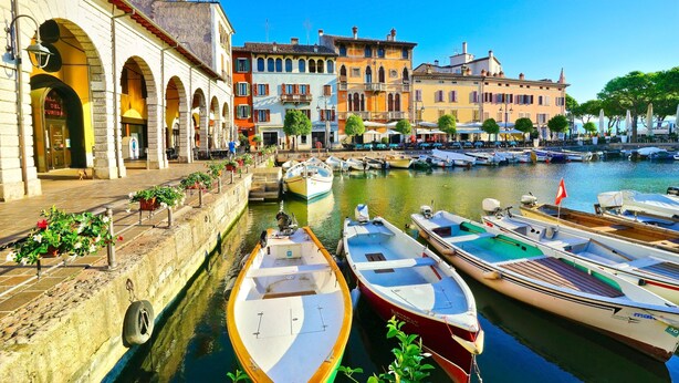 A canal with boats docked, a row of colorful buildings, and a clear blue sky. - Albatros in Dro With 2 Bedrooms and 1 Bathrooms (Dro)
