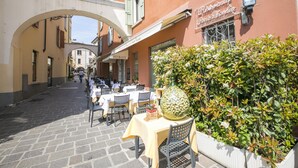 An outdoor café with tables and chairs, a large decorative bottle, and a hedge. - Kristall Lago Pool View (Desenzano del Garda)