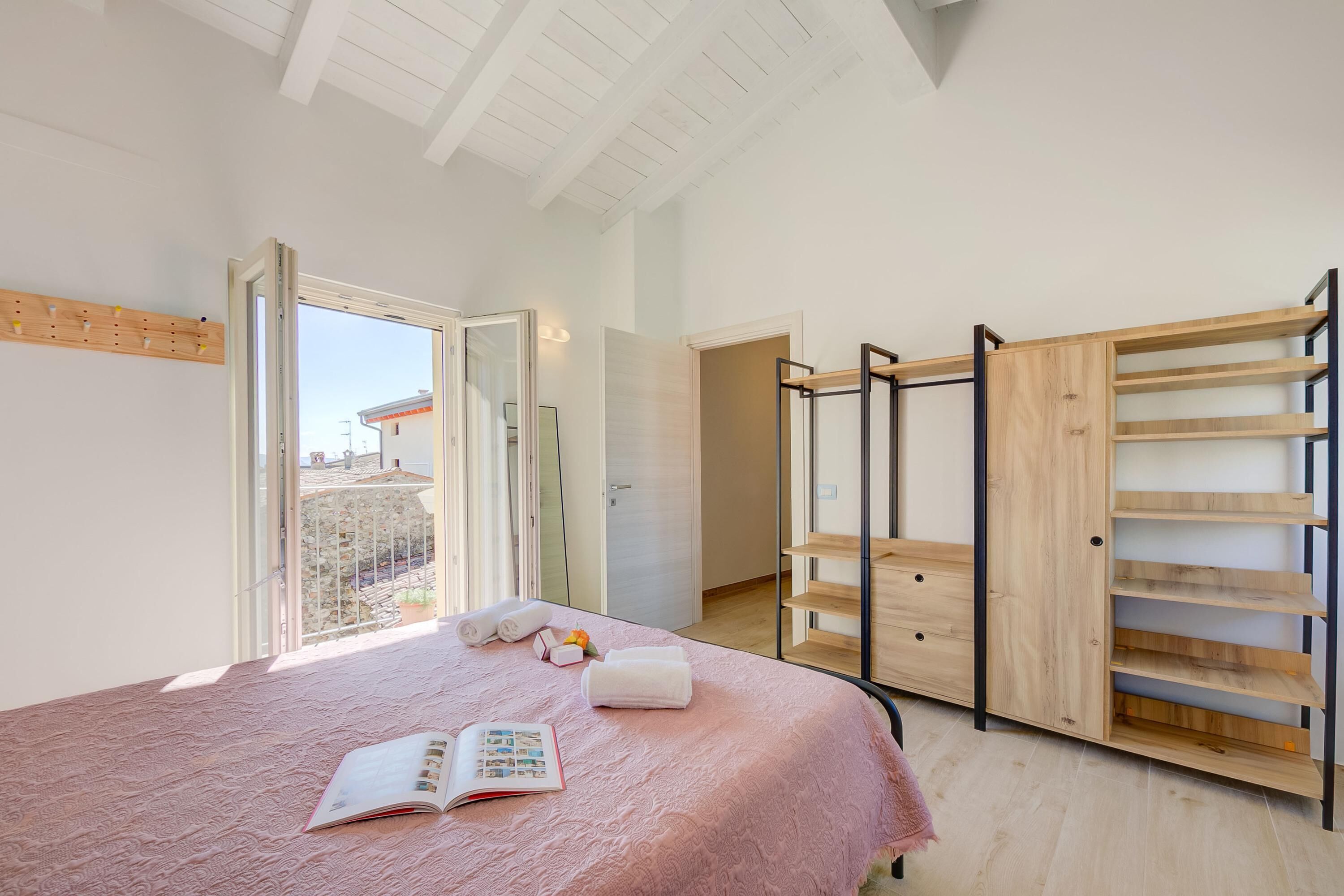 A bedroom with a large bed, a wooden wardrobe, a window with a view, and a ceiling with exposed beams.