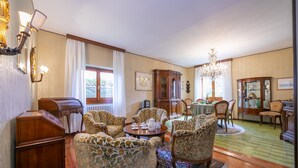 Ein traditionelles Wohnzimmer mit Holzboden, floralen Ohrensesseln, einem Couchtisch, einer Kristallleuchtre und einem Essbereich mit Tisch und Stühlen.