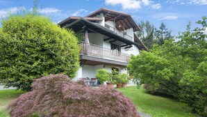 Ein zweistöckiges Haus mit Balkon, umgeben von üppiger Bepflanzung und Topfpflanzen.