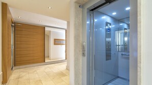 An elevator with a glass door, a wooden panel wall, and a tiled floor. - Bilocale Vista Mare Giorgio (Alghero)
