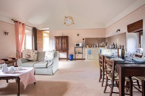A cozy living room with a sofa, a dining table set for four, and a kitchen in the background. - Casale Montemoro With Pool (Allerona)