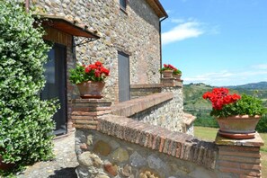 A stone building with a rustic staircase leading to a door, surrounded by potted red flowers and a green bush. - Casale Montemoro With Pool (Allerona)