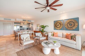 A modern living room with a white sofa, a coffee table, and a dining area with chairs and a table. - Apartment w Pool Ocean View at Punta Palmera BA5 (Punta Cana)