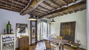 Ein rustikaler Essbereich mit Holztisch und Bänken, einem Weinkühler und einem großen Fenster mit Vorhängen.