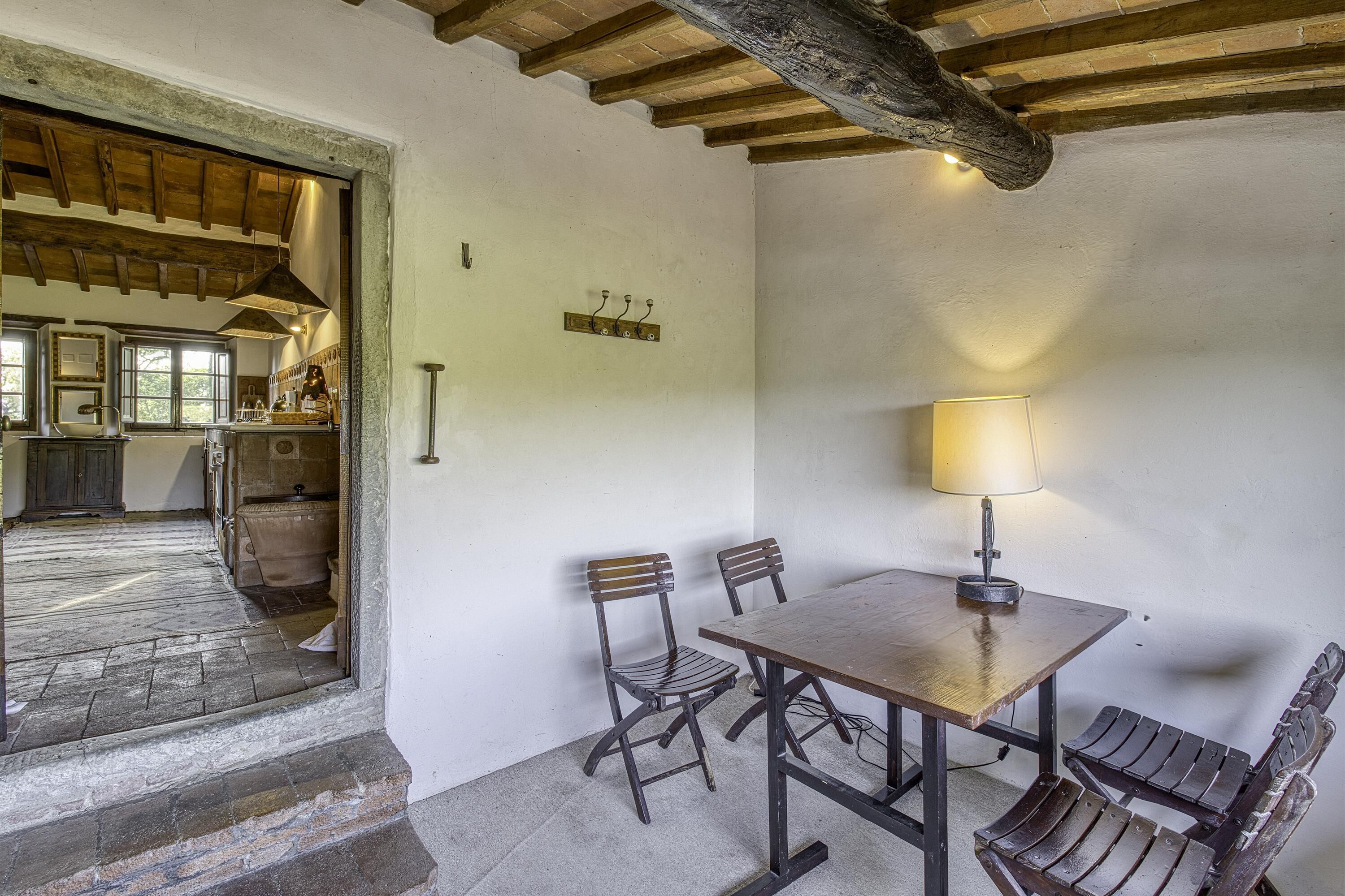 A rustic dining area with a wooden table and chairs, a lamp, and a view into a kitchen through an open doorway.