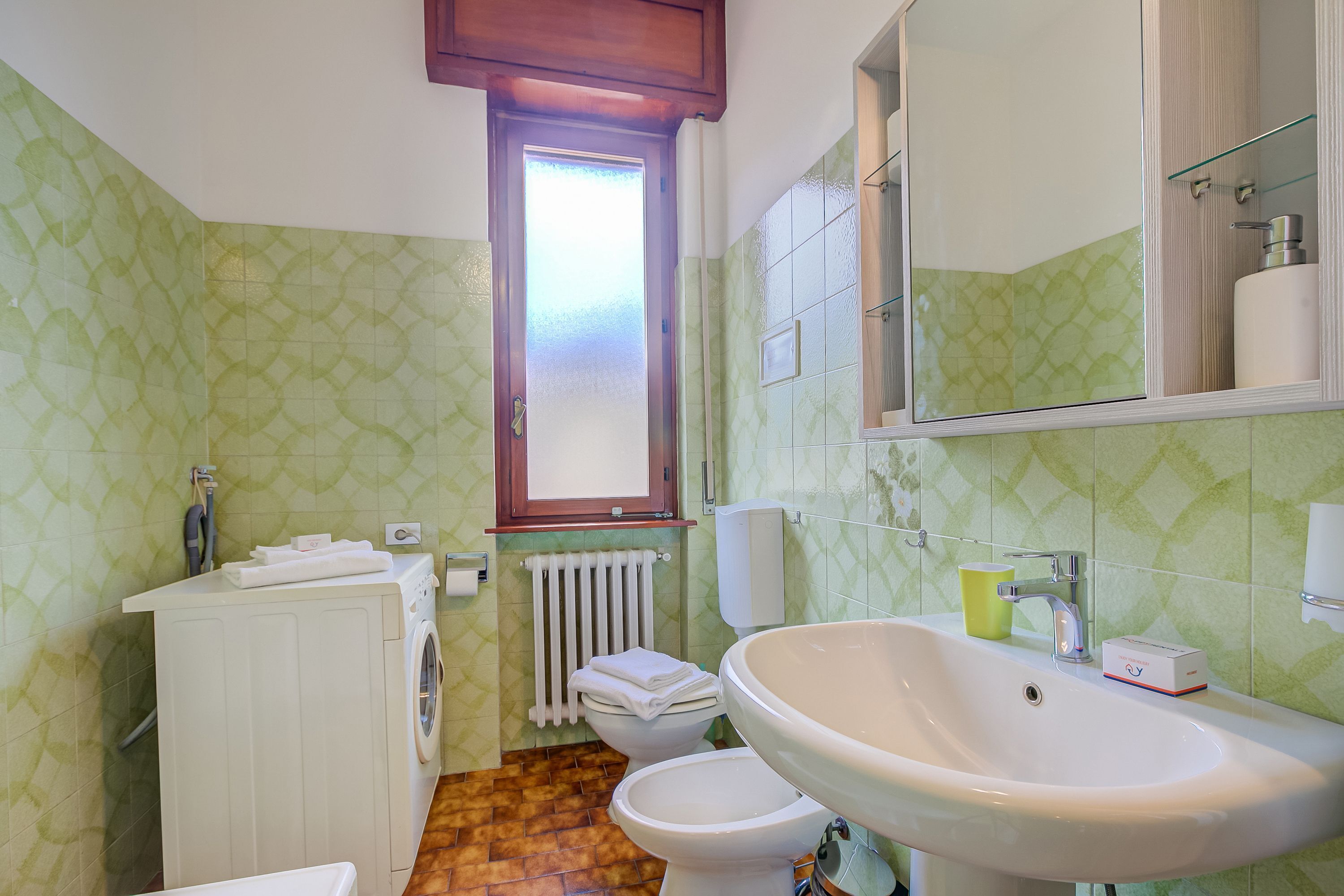 A bathroom with a washing machine, two toilets, a sink, and a mirror.