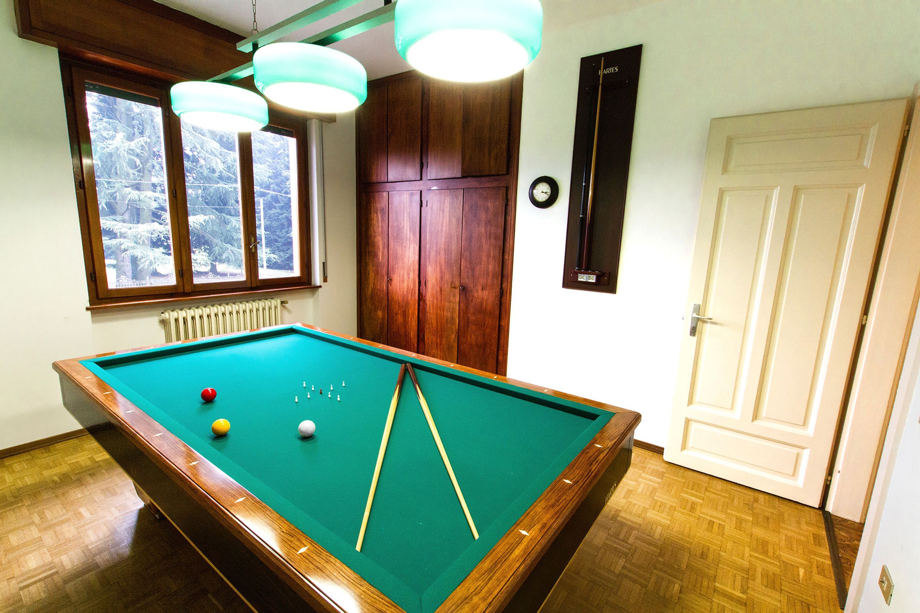 A pool table with balls and cues, wooden cabinets, a clock, and a door.