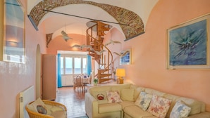 A cozy living room with a beige sofa, wicker chairs, a wooden spiral staircase, and a dining area with a table and chairs. - Il Bijou Di Rossella - Beach Front (Alassio)