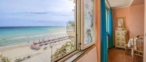 A balcony with a view of a beach, a dining area with a table and chairs, and a cabinet with decorative items.