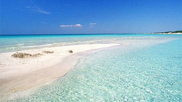 Une plage à l’eau turquoise et limpide, bordée d’un rivage sablonneux.