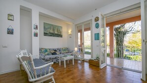 A spacious living room with a sofa, chairs, and a dining table. There is a painting on the wall and a door leading to an outdoor area. - Casa Lavanda Pool Tennis (Ispra)