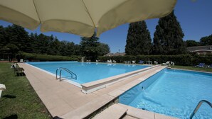 A rectangular swimming pool with a tiled deck, surrounded by lounge chairs and umbrellas. - Casa Lavanda Pool Tennis (Ispra)