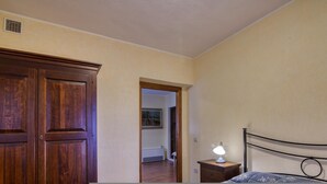 A bedroom with a wooden wardrobe, a bedside table with a lamp, and a bed with a metal headboard. - Appartamento Pera Shared Pool (Roccastrada)