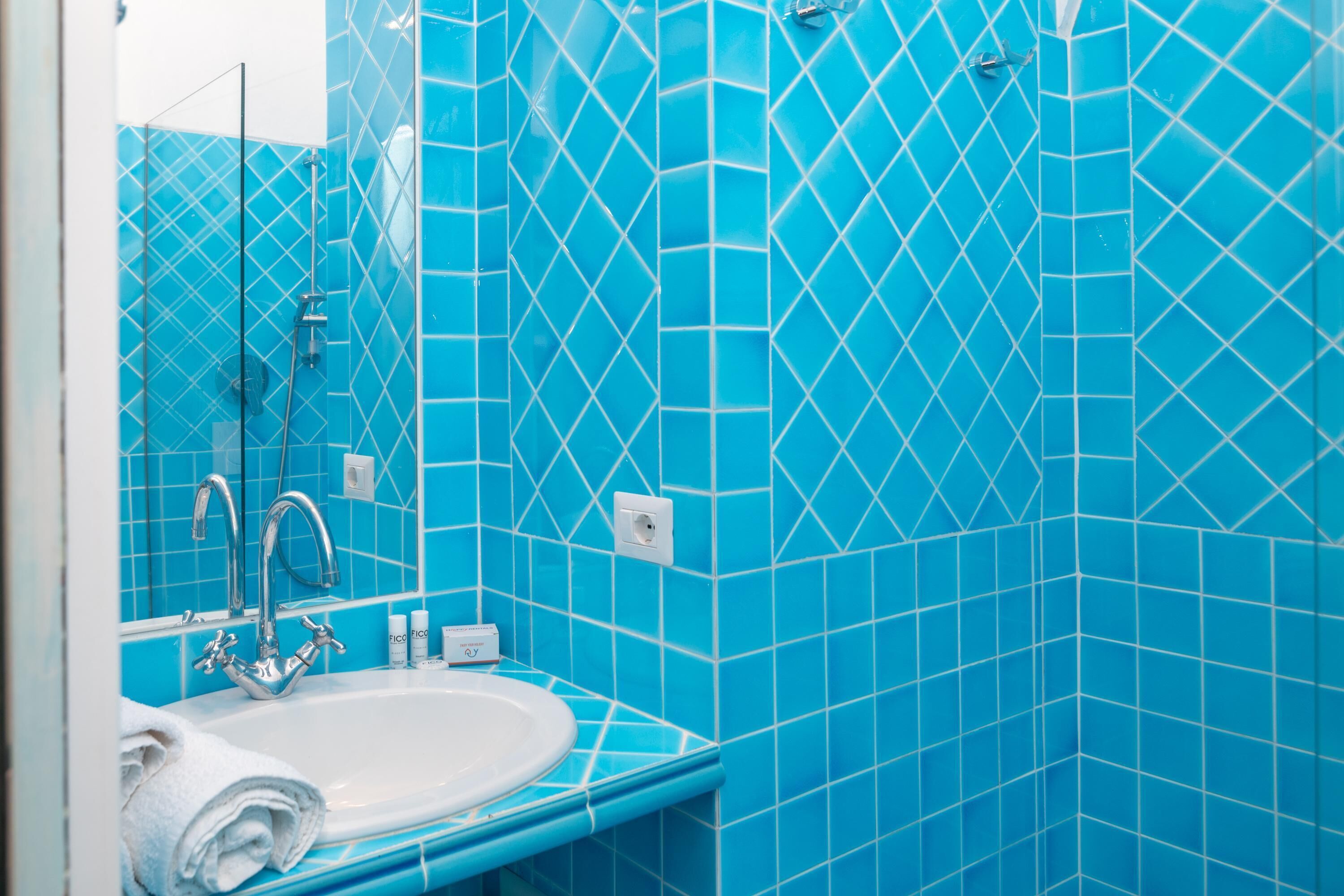 A bathroom with a sink, mirror, and blue-tiled walls.