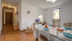 Een eetgedeelte met een tafel voor vier personen, een televisie en een raam met uitzicht op een balkon.