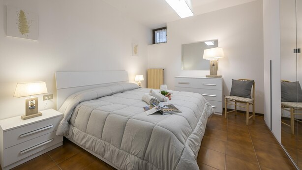 Een slaapkamer met een bed, nachtkastjes, een stoel, een kaptafel, een spiegel en een raam.