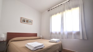 A hotel room with a bed, a nightstand, a lamp, and a window with curtains. - Le Dimore di Nettuno 4 With Pool (Olbia)