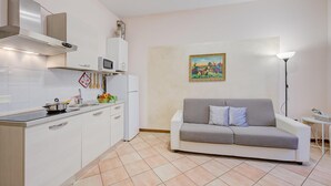 A modern kitchen with white cabinets, a microwave, and a stove. There is a gray sofa and a painting on the wall. - Berny 150m From Lake (Salò)