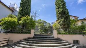 A set of outdoor stone steps leading up to a building, surrounded by tall trees and a clear blue sky. - Berny 150m From Lake (Salò)