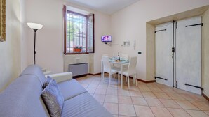 A living room with a sofa, a dining table with chairs, a TV, and a window with a view. - Berny 150m From Lake (Salò)